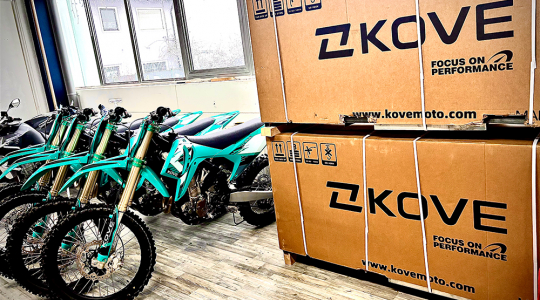 Mehrere türkisfarbene Offroad-Motorräder stehen neben großen KOVE-Transportkisten in einem Raum.